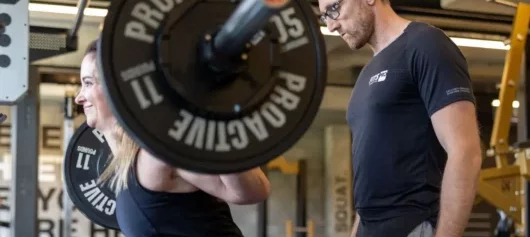 Squat dans une salle de sport avec un coach sportif - FITSPRO